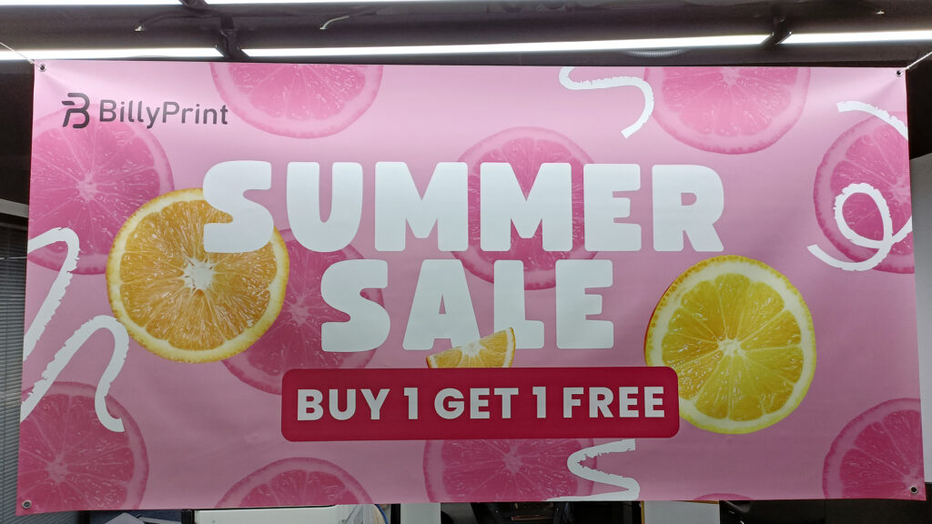 Wide view of a pink double-sided vinyl banner by BillyPrint with 'SUMMER SALE, BUY 1 GET 1 FREE' offer, featuring lemon and lime graphics.