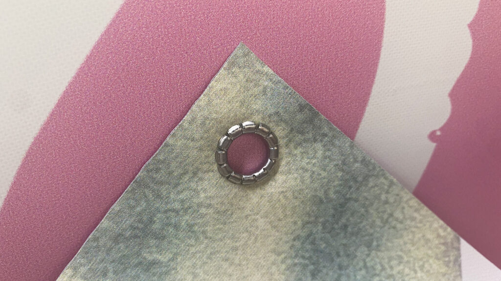 Detail of the corner of a pink double-sided vinyl banner showing the eyelet and reinforced edge.